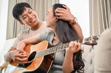 Sevimli ve mutlu bir Asyalı çift evlerinde bir kanepede gitar çalıyor, güzel anılar yaratıyor ve eğleniyorlar. erkek ve kız arkadaş, ev hayatı