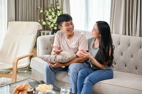 Happy young Asian couple enjoy talking on a sofa in the living room, spending happy weekend together at home.