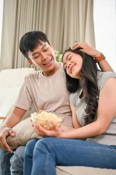 Happy, lovely young Asian couple spending a romantic time at home together, watching a movie in the living room. caring husband and cute wife