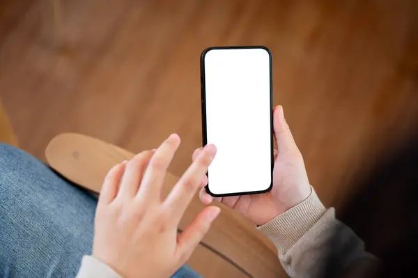 A white screen smartphone mockup to display your graphic ads is in a woman\'s hand. A woman is sitting on a chair indoors and using her smartphone. people and wireless technology