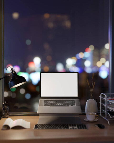 A white-screen laptop computer mockup on a computer stand and office supplies on a desk against the window with a night city view. office at night. 3d render, 3d illustration