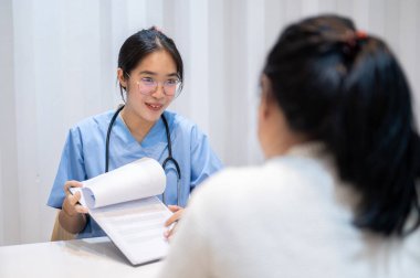 Profesyonel ve deneyimli bir Asyalı kadın doktor hastanedeki sağlık kontrolü sırasında bir hastaya rapor veriyor ve tavsiyelerde bulunuyor. Halk ve sağlık kavramları