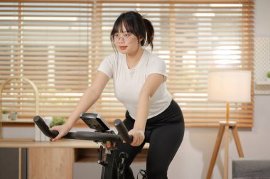 Güçlü ve formda bir Asyalı kadın spor kıyafetleriyle spor yapıyor. Spor bisikletinde egzersiz yapıyor. Evde kardiyo yapıyor. insanlar ve kapalı spor kavramları