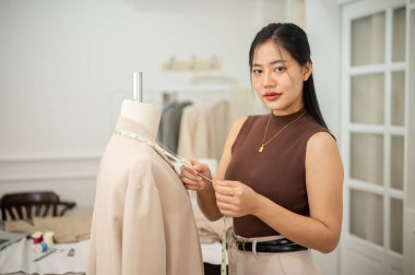 Profesyonel ve kendine güvenen Asyalı bir kadın terzi stüdyosunda çalışıyor. Giysilerini ve ölçülerini ayarlıyor. Bir terzi mankeninin ölçüm bandıyla..