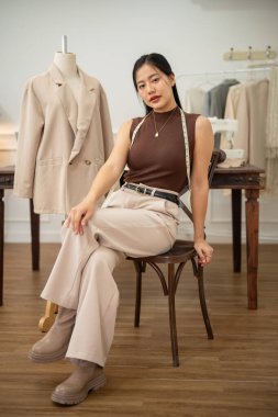 Kendine güvenen ve çekici bir Asyalı kadın moda tasarımcısı ya da terzi stüdyosunda bir sandalyede oturmuş kameraya bakıyor. insanlar ve moda kavramları