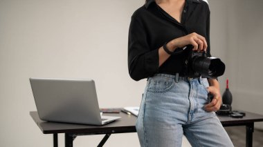 Siyah gömlekli, kendine güvenen profesyonel bir kadın fotoğrafçı elinde DSLR kamerasıyla fotoğraf stüdyosunda duruyor..
