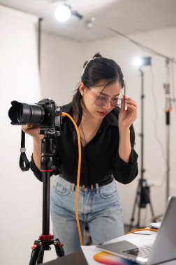 Havalı, profesyonel bir Asyalı kadın fotoğrafçı dizüstü bilgisayarındaki görüntüleri kontrol ediyor. Stüdyoda profesyonel fotoğraf ekipmanlarıyla çalışıyor..