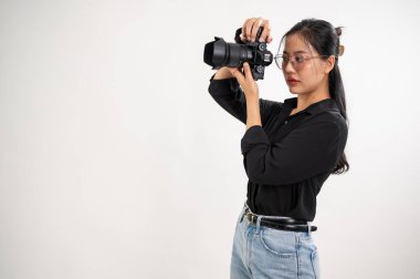 Siyah gömlekli profesyonel, kendine güvenen bir Asyalı kadın fotoğrafçı elinde profesyonel bir DSLR kamerasıyla bir fotoğraf stüdyosunda fotoğraf çekiyor..