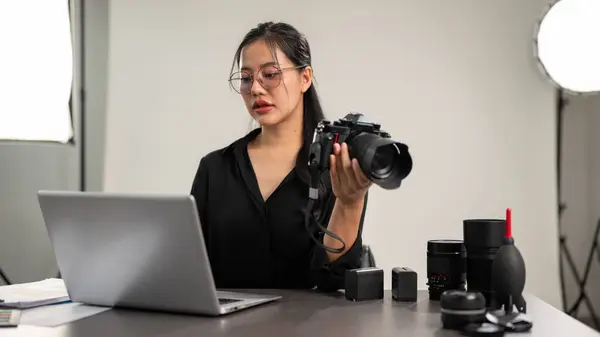 A professional, elegant Asian female photographer in a black shirt is focusing on checking images on her laptop computer, working in a studio.