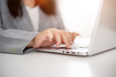 Bilgisayarda çalışan ya da gezinen bir iş kadınının kırpılmış bir görüntüsü, elleri dizüstü bilgisayarda yazan, modern, parlak bir ofiste çalışan.