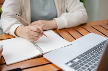 Günlük kıyafetlerle gezen bir kadın dış mekanda çalışırken deftere bir şeyler yazıyor ya da not alıyor..