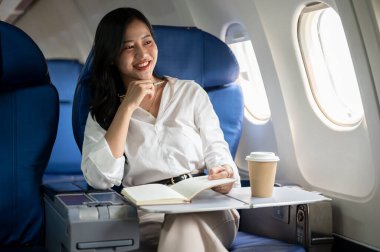 Çekici bir Asyalı iş kadını pencerenin dışındaki manzaraya bakıyor, bir uçakta pencere kenarında oturuyor, iş gezisine çıkıyor. İş insanları ve ulaşım kavramları