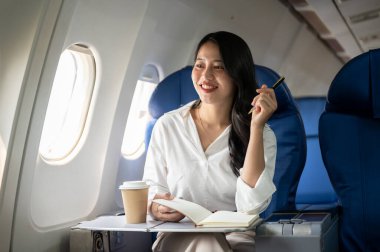 Çekici bir Asyalı iş kadını pencerenin dışındaki manzaraya bakıyor, bir uçakta pencere kenarında oturuyor, iş gezisine çıkıyor. İş insanları ve ulaşım kavramları