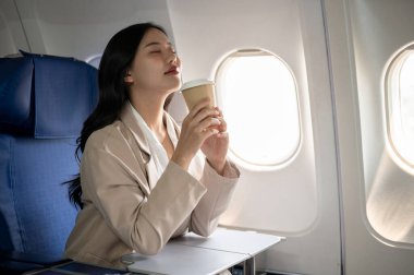 Resmi takım elbiseli çekici, rahat Asyalı bir iş kadını gözlerini kapalı tutar, uçuş sırasında kahvesinin tadını çıkarır, iş seyahati için uçakla seyahat eder. Lüks hayat tarzı, iş insanları.