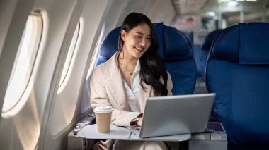 Çekici, başarılı Asyalı bir iş kadını ya da takım elbiseli bir kadın CEO başka bir şehre yaptığı iş gezisi sırasında dizüstü bilgisayarı üzerinde çalışıyor. uçak, ulaşım