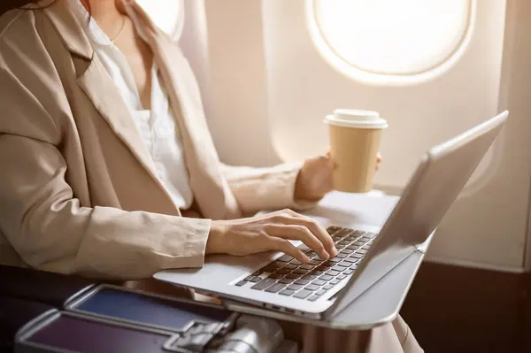 A cropped image of a hard-working businesswoman in a business suit is working on her laptop computer during the flight, flying to another city for a business meeting. working remotely, airplane mode