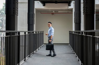 Kendine güvenen, deneyimli bir Asyalı işadamı elinde kahve fincanı ve çantayla bir şirket koridorunda kameraya gülümsüyor. iş insanları konsepti