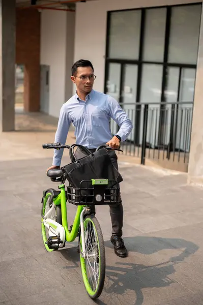 A focused and determined Asian millennial businessman pushing a green bicycle in the city, going to work with his bicycle on a sunny day. businesspeople and sustainable transportation concepts