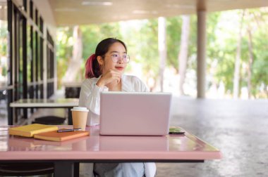 Üniversite kantininde ya da kafeteryasında otururken dizüstü bilgisayarı üzerinde çalışan genç bir Asyalı kız öğrenci. üniversite hayatı ve teknoloji kavramları
