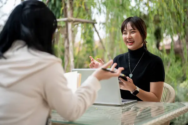 A cheerful young Asian woman in casual clothes talking with her friend while working remotely in the garden. discussion, interview, meeting