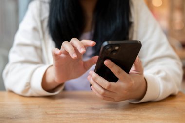Sıradan giyinmiş Asyalı bir kadının kapalı bir masada akıllı telefonunu kullanırken çekilmiş görüntüsü. İnsanlar ve kablosuz teknoloji kavramları