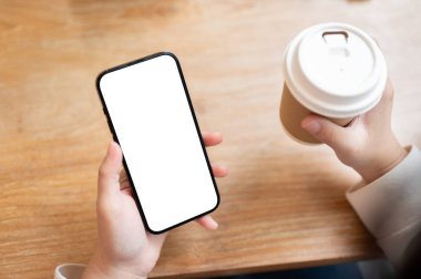 Kapalı bir masada elinde akıllı telefon ve kahve fincanı tutan bir kadının yakın plan görüntüsü. Grafik reklamlarını görüntülemek için beyaz ekran akıllı telefon modeliName.