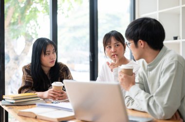 Bir grup Asyalı üniversite öğrencisi çalışma alanında otururken ya da sınıfta birlikte ders çalışırken iş ve fikirlerini paylaşıyorlar. Eğitim ve arkadaşlık kavramları