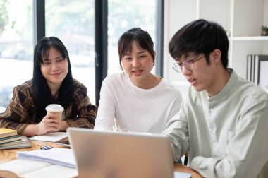 Bir grup Asyalı üniversite öğrencisi çalışma alanında otururken ya da sınıfta birlikte ders çalışırken iş ve fikirlerini paylaşıyorlar. Eğitim ve arkadaşlık kavramları