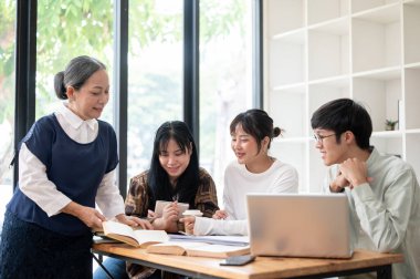 Olumlu ve nazik bir kıdemli Asyalı bayan öğretmen sınıfta öğrencilerine öğretiyor. Yetişkin bir bayan profesörle çalışan bir grup üniversite öğrencisi. eğitim kavramı