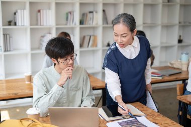 Yetişkin bir Asyalı bayan öğretmen, sınıftaki öğrencisine zor matematik problemlerini açıklamaya yardım ediyor. eğitim kavramı