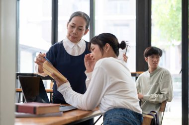 Son sınıf Asyalı kadın öğretmen, sınıftaki öğrencisine zor matematik problemlerini açıklamaya yardım ediyor. eğitim kavramı