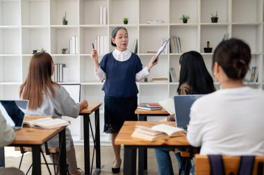 Profesyonel ve deneyimli bir Asyalı bayan öğretmen ya da profesör sınıfta öğrencilere ders veriyor, bir dersi anlatıyor, sınıfın önünde duruyor. Eğitim kavramı