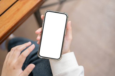 Kapalı bir masada akıllı telefonunu kullanan, günlük giysiler içindeki bir kadının yakın plan görüntüsü. Grafik reklamları için beyaz ekran akıllı telefon modeli. İnsanlar ve kablosuz teknoloji kavramları