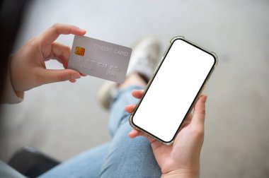Kredi kartı ve akıllı telefon tutan bir kadının kapalı mekanda otururken çekilmiş yakın plan görüntüsü. Bulanık bir geçmişi olan bir kadının elinde beyaz ekran akıllı telefon modeli. Online alışveriş, mobil bankacılık