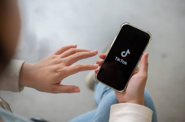 Chiang Mai, Tayland - 07 Mayıs 2024: Kot pantolonlu bir kadının yakın plan görüntüsü evde oturuyor ve akıllı telefonunda TikTok uygulamasını kullanıyor. insanlar ve sosyal medya platformları