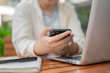 Şehirdeki bir kafede çalışan, bilgisayarını tamir ederken akıllı telefonunu kullanan, gündelik giysili genç bir Asyalı kadının kırpılmış görüntüsü..