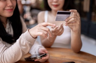 İki mutlu Asyalı bayan arkadaş, kentteki bir kafe veya restoranın açık masasında otururken kredi kartlarının faydalarından bahsedip, yemek faturalarını kredi kartıyla ödüyorlar..