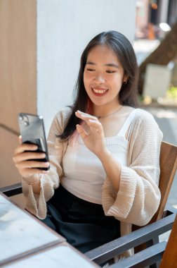 Neşeli bir Asyalı kadın, şehirdeki bir restoranda dinlenirken arkadaşıyla telefonuyla video görüşmesi yapmaktan hoşlanıyor. İnsanlar, yaşam tarzı ve kablosuz teknoloji kavramları