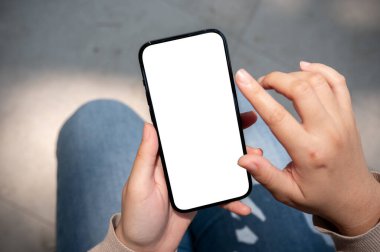 Güneşli bir günde dışarıda oturan ve akıllı telefonunu ekranda dokunurken ya da yazarken kullanan bir kadının yakın plan görüntüsü. Beyaz ekran akıllı telefon modeli, bir kadının elindedir. İnsanlar ve kablosuz teknoloji