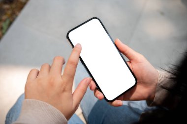 Güneşli bir günde dışarıda oturan ve akıllı telefonunu ekranda dokunurken ya da yazarken kullanan bir kadının yakın plan görüntüsü. Beyaz ekran akıllı telefon modeli, bir kadının elindedir. İnsanlar ve kablosuz teknoloji