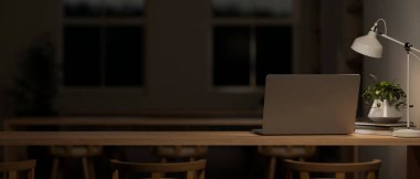 Geceleri karanlık bir sınıf ya da ortak çalışma alanında bir dizüstü bilgisayar, dekor ve masa lambasının loş ışığı yer alır. Arka plan görüntüsünü kapat. 3d görüntüleme, 3d illüstrasyon