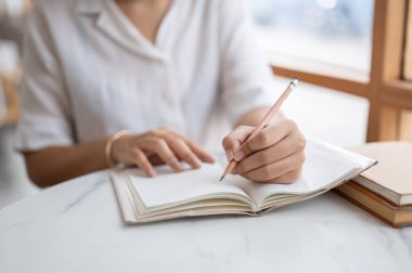 Beyaz gömlekli bir kadının kalem tutarken, defterine bir şeyler yazarken, günlüğünü tutarken, bir kafede otururken fikir ve liste yaparken çekilmiş bir fotoğrafı..