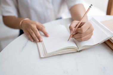 Beyaz gömlekli bir kadının kalem tutarken, defterine bir şeyler yazarken, günlüğünü tutarken, bir kafede otururken fikir ve liste yaparken çekilmiş bir fotoğrafı..