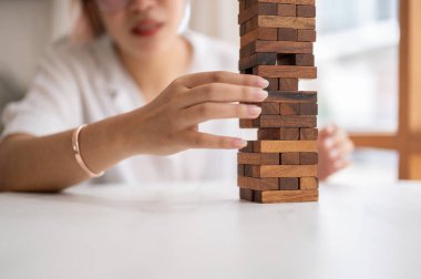 Bir kadının yakın plan çekimi, dikkatini bir masada ahşap blok oyunu oynamaya, tahta bir bloğu hareket ettirmeye verir. oyuncak, oyun, eğlence