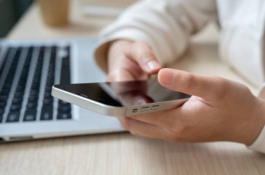 Ofis masasında akıllı telefonunu kullanan, mesajları kontrol eden ya da mobil uygulama kullanan bir kadının yakın plan görüntüsü. İnsanlar ve kablosuz teknoloji kavramları