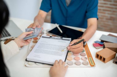 Bir kadın müşterinin yakın plan görüntüsü, bir ev inşaatı sözleşmesi imzalamak ve ofisteki toplantı sırasında müteahhitine veya iç mimarına para ödemektir..