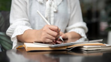 Stilus kalem tutan, dijital tabletine yazı yazan ya da resim çizen, şehirdeki bir kafeden uzaktan çalışan bir kadının kırpılmış görüntüsü. İnsanlar ve kablosuz teknoloji kavramları