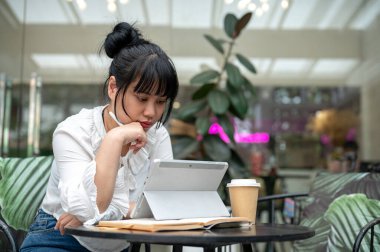 Dijital tabletinden bir şeyler okuyan genç bir Asyalı kadın şehirdeki bir kahve dükkanında çalışıyor. İnsanlar ve kablosuz teknoloji kavramları