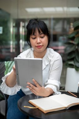 Dijital tabletinden bir şeyler okuyan genç bir Asyalı kadın şehirdeki bir kahve dükkanında çalışıyor. İnsanlar ve kablosuz teknoloji kavramları