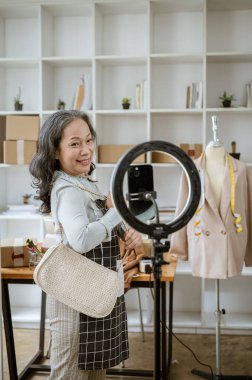 Çekici olgun bir Asyalı kadın çevrimiçi satıcı evinden canlı yayın yapıyor, ürünlerini sosyal medya üzerinden satıyor ya da akıllı telefonuyla bir ürün değerlendirme videosu kaydediyor..